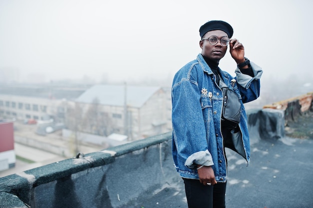 Homem afro-americano na boina de jaqueta jeans e óculos posou no telhado abandonado