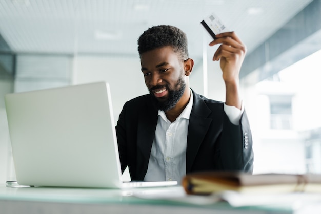 Homem afro-americano que paga com cartão de crédito on-line ao fazer pedidos via internet móvel, fazendo transações usando o aplicativo do banco móvel.