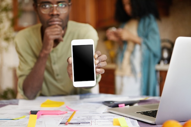 Homem afro-americano sério usando óculos, segurando um celular