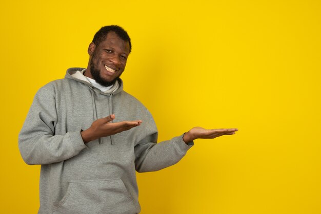 Homem afro-americano sorridente que abriu as mãos, em frente à parede amarela.