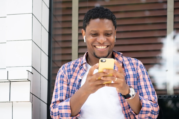 Homem afro-americano, usando seu telefone celular enquanto está sentado em uma vitrine na rua. conceito urbano.