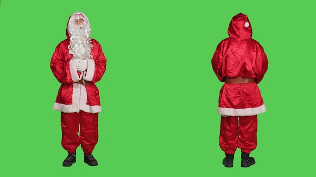 Foto grátis homem agindo como papai noel fantasiado dizendo ho ho ho, retratando o famoso personagem de dezembro para a celebração da véspera de natal. são nicolau com chapéu e barba em cima da tela verde de corpo inteiro.