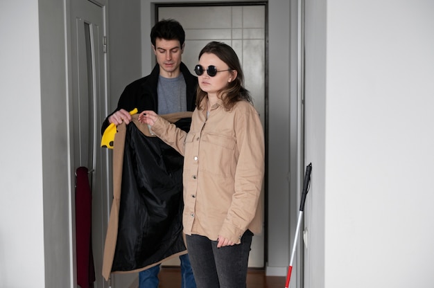 Homem ajudando uma mulher cega a vestir o casaco