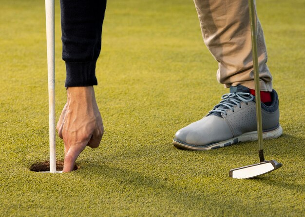 Homem alcançando o buraco da bola de golfe com a mão