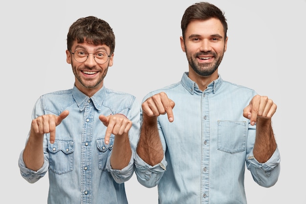 Homem alegre, companheiros com expressões positivas, apontar para baixo, envolvido em propaganda, vestido com roupas casuais