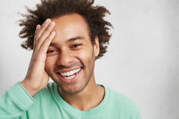 Homem alegre de pele escura e penteado afro com as mãos na cabeça, rindo e se divertindo