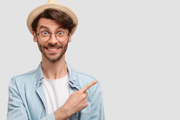 Homem alegre e próspero agricultor com roupas casuais casuais, indica à parte como mostra seu lindo jardim com muitas plantas, sente-se orgulhoso, trabalhando duro, tem expressão feliz