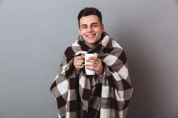 Homem alegre em manta quente, segurando o chá quente