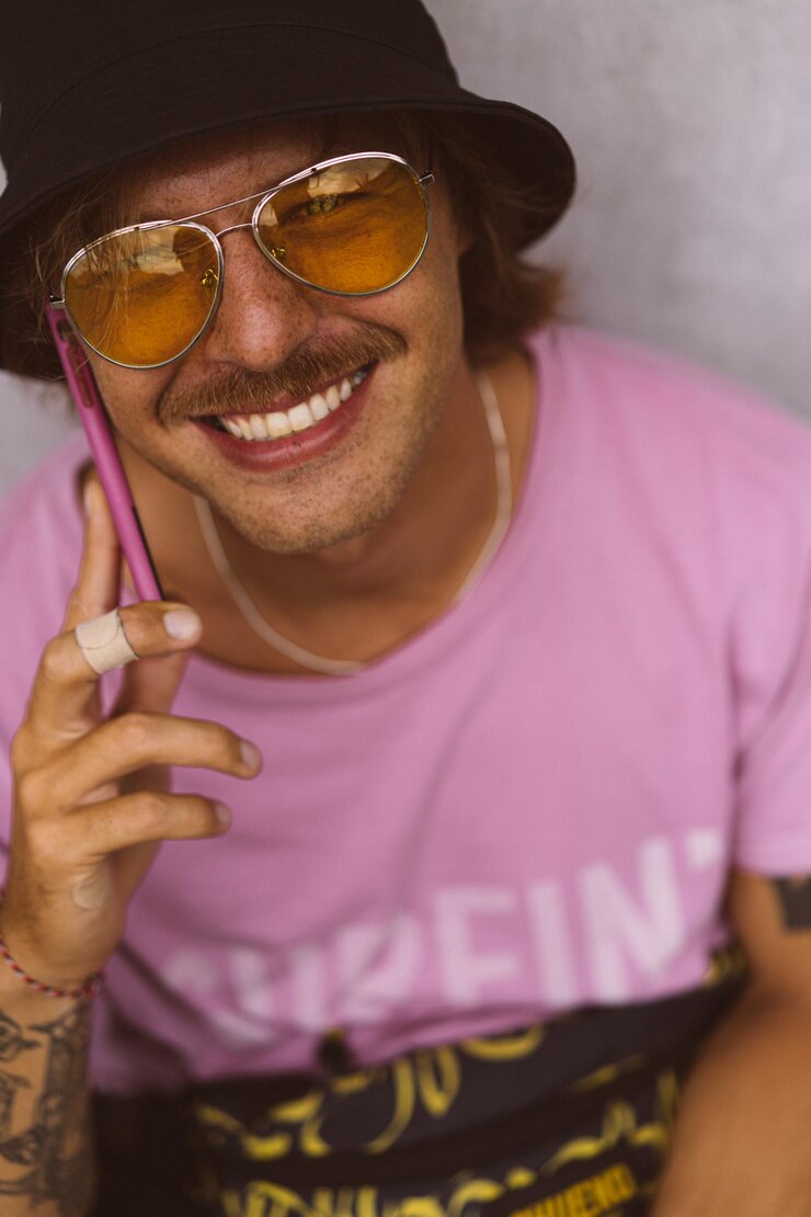 Foto grátis homem alegre feliz em óculos de sol amarelos, panamá e camiseta brilhante sorri, ri, usa telefone, liga para amigos, escreve uma mensagem nas redes sociais. hipster, hippie, pessoas brilhantes coloridas.