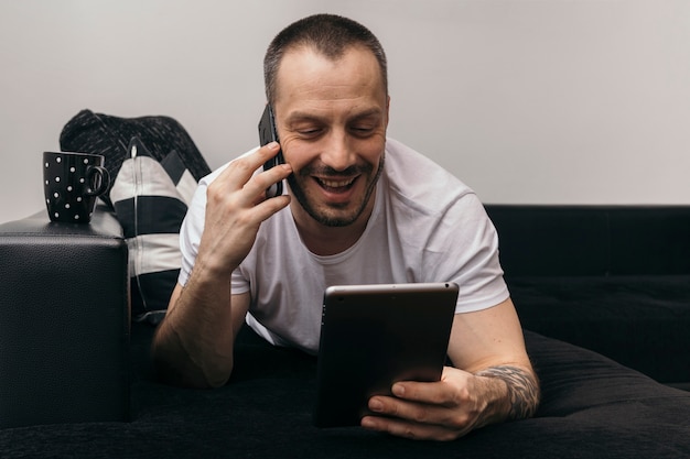 Homem alegre navegando tablet e falando no telefone