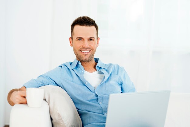 Homem alegre relaxando com laptop e uma xícara de café