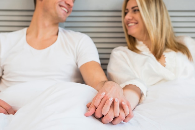 Homem alegre, segurando mão, de, mulher jovem, cama