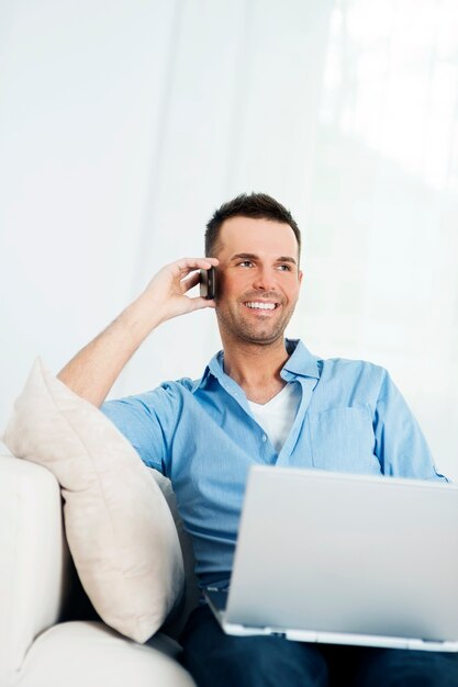 Homem alegre usando laptop e falando no celular