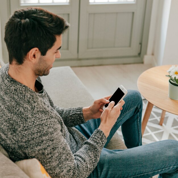 Homem alegre usando smartphone no sofá