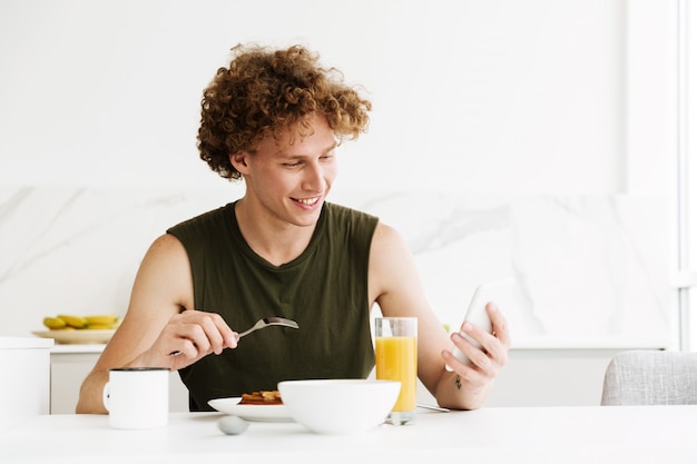 Homem alegre, usando telefone celular e comer bolos