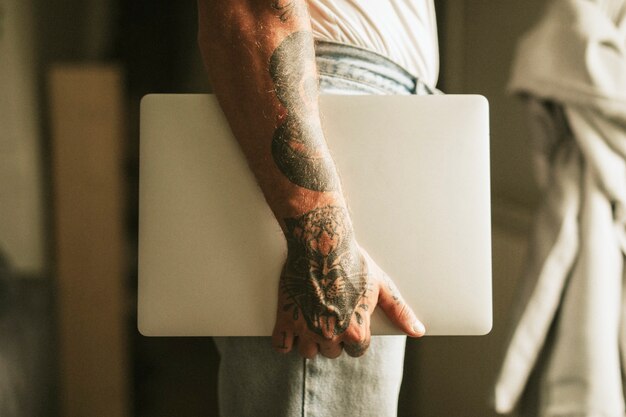 Homem alternativo tatuado carregando um laptop