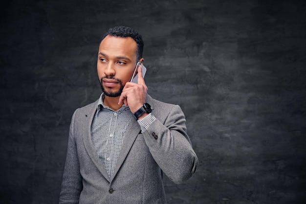 Homem americano preto barbudo elegante em um terno cinza fala no telefone inteligente.