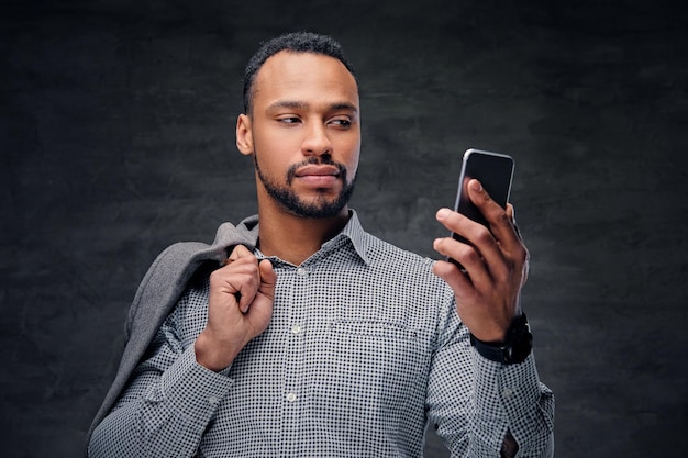 Homem americano preto casualmente vestido detém telefone inteligente sobre fundo cinza vinheta.