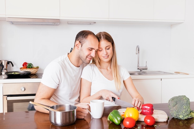 Homem amoroso sentado com sua esposa, cortando os legumes com faca