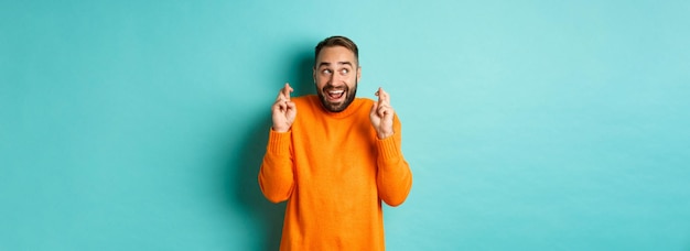 Foto grátis homem animado esperando algo com antecipação, mantenha os dedos cruzados e sorrindo, fazendo o desejo ficar