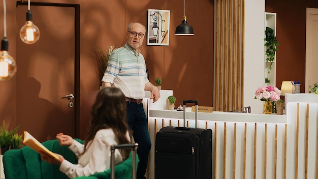 Homem aposentado tocando campainha de serviço para fazer check-in na recepção do hotel, chegando ao resort de luxo de férias. pessoa em idade de reforma que viaja de férias no estrangeiro, funcionários da recepção. tiro de tripé.