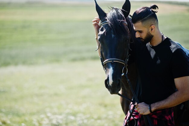 Homem árabe de barba alta usa preto com cavalo árabe