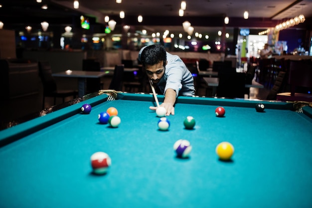 Homem árabe elegante usar jeans jogando bilhar no bar.