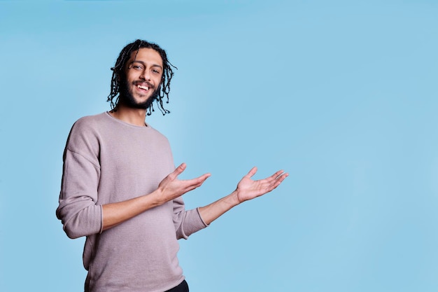 Foto grátis homem árabe sorridente apontando com as mãos para o lado enquanto anuncia o produto e olhando para a câmera. pessoa alegre com expressão facial positiva mostrando à esquerda com retrato de braços