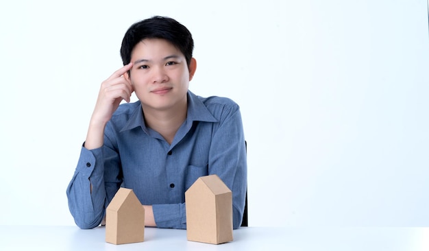 Homem asiático inteligente de negócios com modelo de casa no fundo branco de dicisão de negócios de casa de mesa