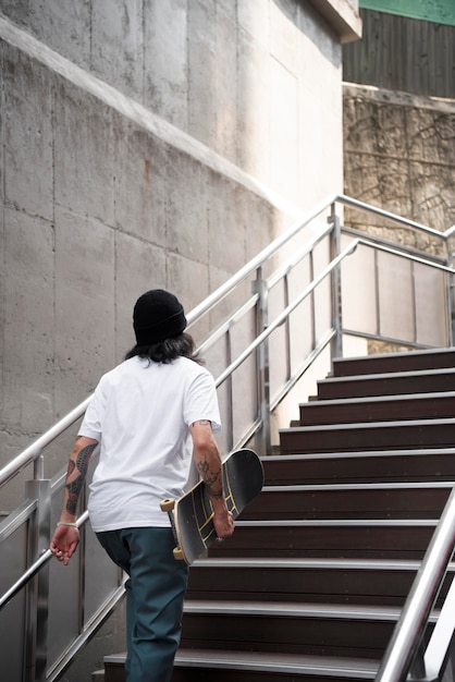 Homem asiático segurando seu skate enquanto caminha na escada