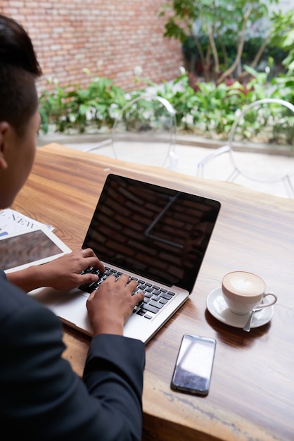 Homem asiático trabalhando no laptop no café ao ar livre do jardim