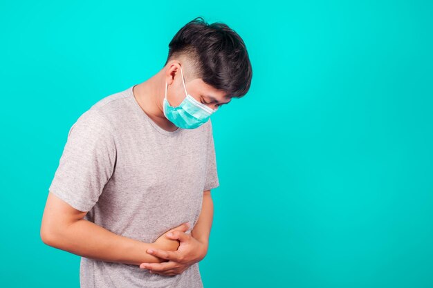 Homem asiático usa uma camiseta com dor de estômago porque está com diarreia sobre fundo verde
