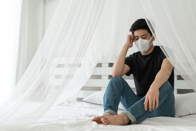 Homem asiático usando máscara facial para evitar dores de cabeça e tosse devido ao Coronavírus covid-19 na sala de quarentena