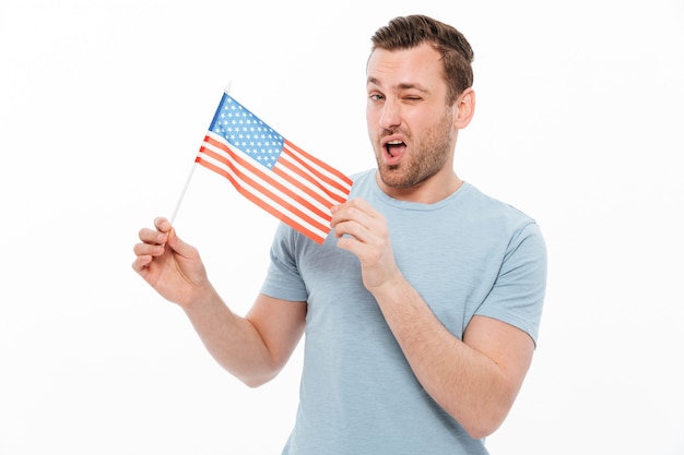 homem atraente com cerdas demonstrando positivamente a pequena bandeira americana e piscando