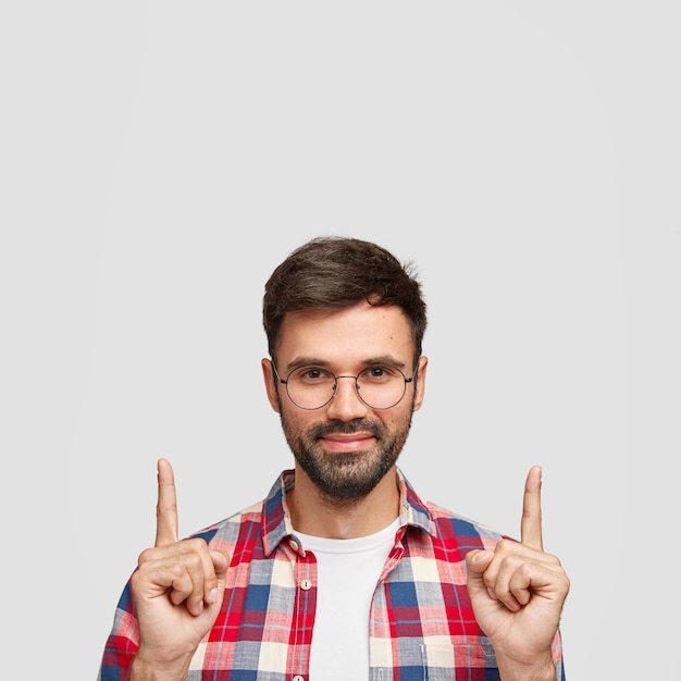 Homem atraente com cerdas escuras, usa camisa casual, indica com o dedo indicador para cima