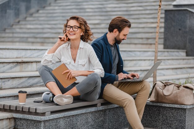 Homem atraente e mulher sentada em uma escada no centro urbano da cidade, trabalhando juntos em um laptop