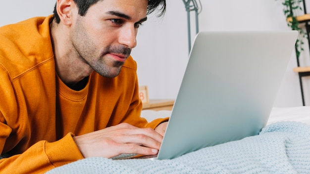 Foto grátis homem atraente que procura laptop na cama