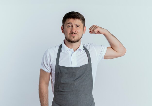 Homem barbeiro com avental olhando para a câmera levantando o punho com expressão confiante, conceito vencedor em pé sobre um fundo branco