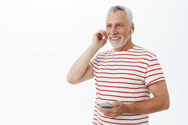Homem barbudo adulto bonito e sorridente usando fones de ouvido sem fio e smartphone
