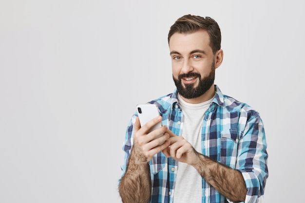 Foto grátis homem barbudo adulto fazendo pedidos on-line usando o telefone celular