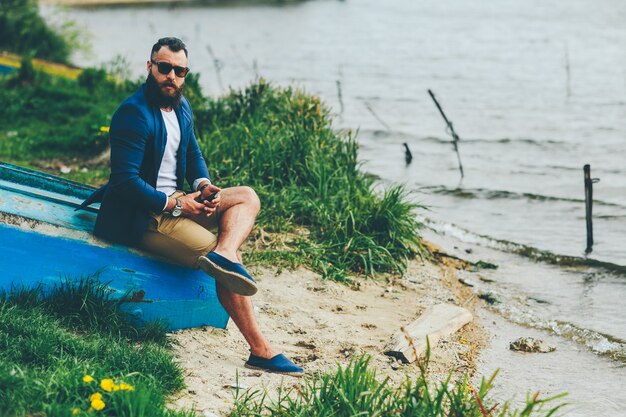 Homem barbudo americano parece na margem do rio com uma jaqueta azul