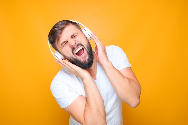 Homem barbudo com fones de ouvido musicais brancos ouve música e canta ao mesmo tempo.