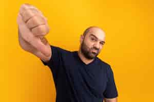 Foto grátis homem barbudo com uma camiseta azul marinho descontente mostrando os polegares para baixo em pé sobre a parede laranja