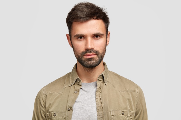 Foto grátis homem barbudo confiante com cabelo escuro, expressão facial séria, pensa no futuro emprego, vestido com uma camisa da moda