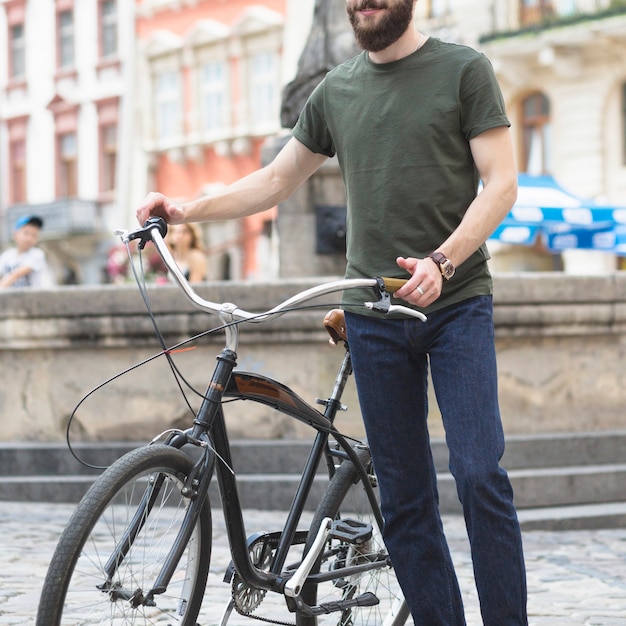 Homem barbudo de pé com sua bicicleta na cidade