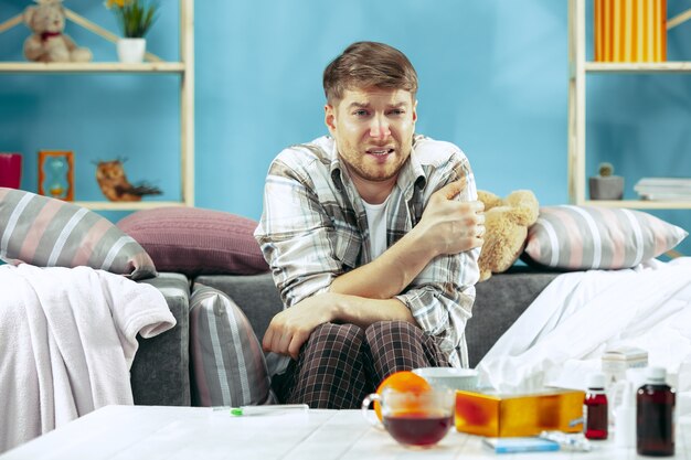 Homem barbudo doente com gripe sentado no sofá em casa.