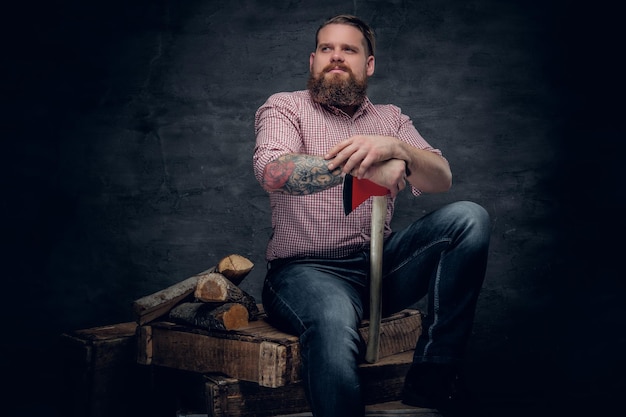 Foto grátis homem barbudo elegante com tatuagens nos braços vestindo camisa xadrez rosa e segura um machado.