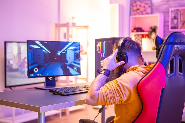 Foto grátis homem barbudo jogando videogame online em seu pc e conversando com outros jogadores. neons coloridos na sala.