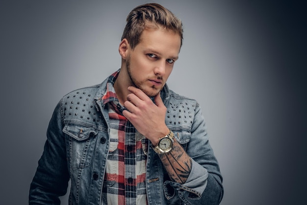 Homem barbudo loiro positivo vestido com uma camisa xadrez e jaqueta jeans posando no fundo cinza da vinheta.