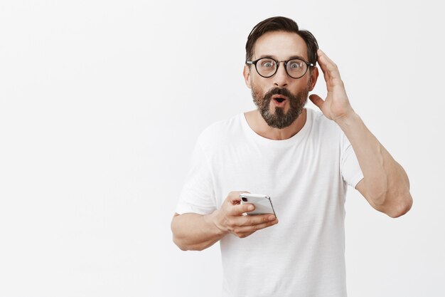 Homem barbudo maduro e animado posando com seu telefone